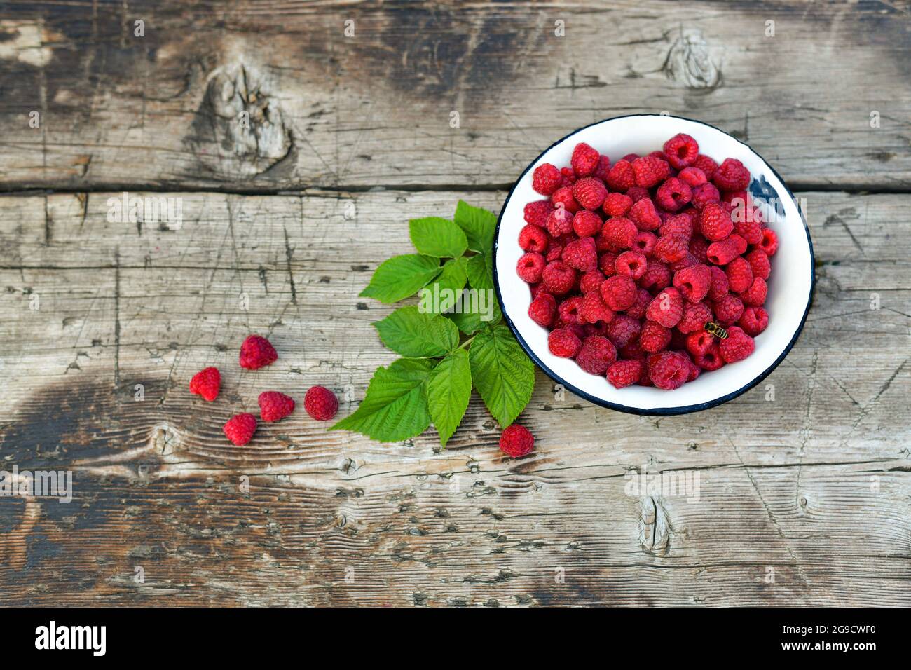 Fresh raspberries in a bowl on a wooden background. Berries and leaves. Stock Photo