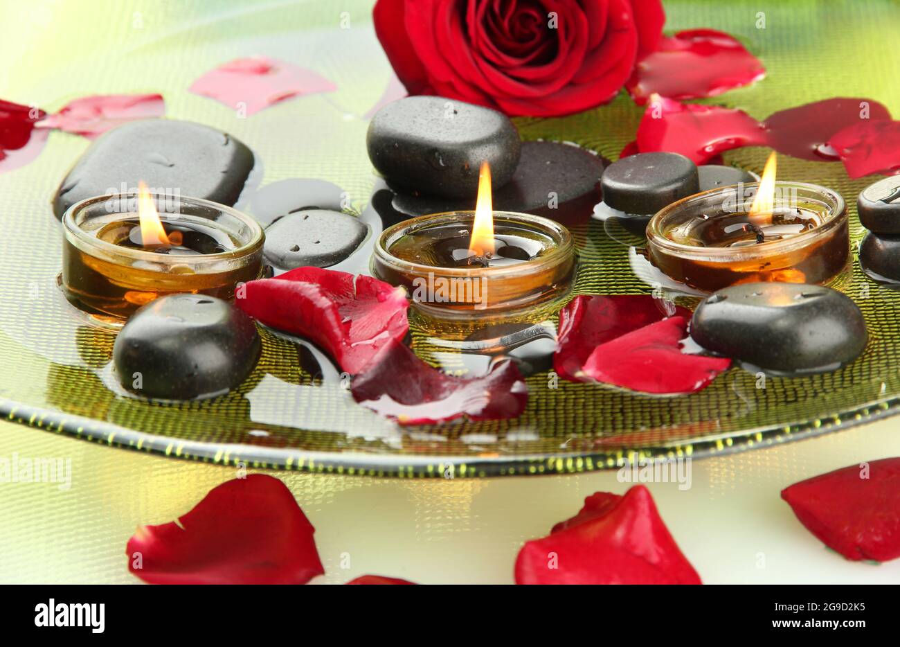 spa stones with rose petals and candles in water on plate Stock Photo ...