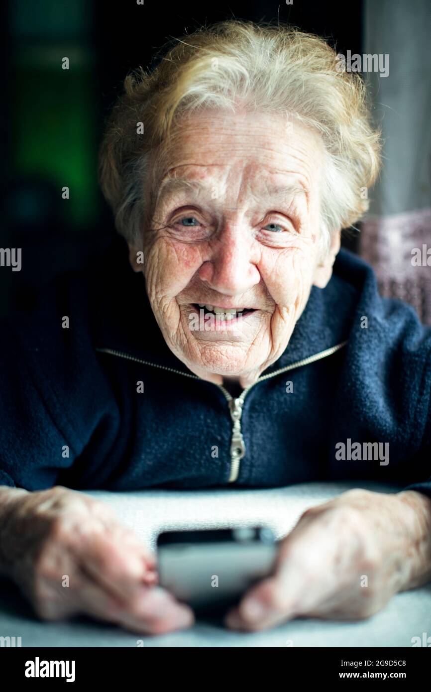 Portrait of senior woman sitting at table typing on a smartphone. Stock Photo