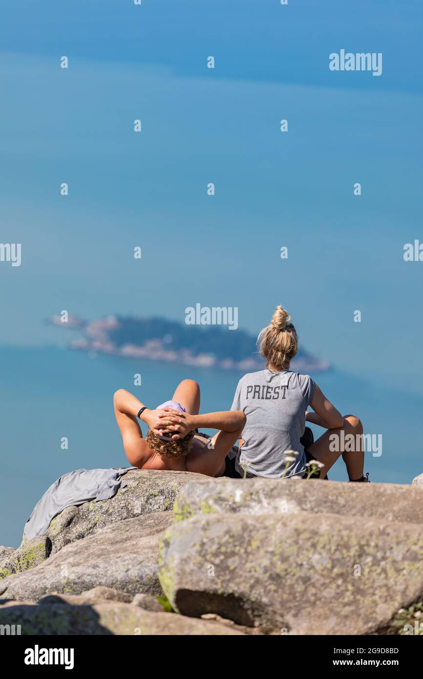 Rare view of a young couple sitting on a big rock while looking far on the beautiful landscape of the sea and islands. Cypress Provincial Park, Stock Photo