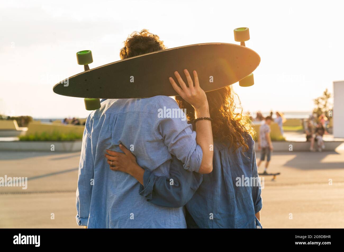 Romantic couple of skateboarders enjoy sunset embracing with longboard in hands in urban skate park Stock Photo