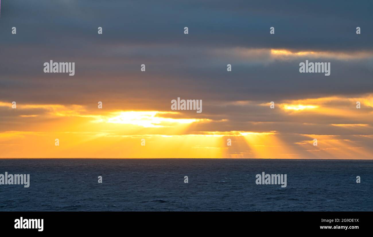 Sun rays passing through dark clouds. The unpredictable drama of the sky at sunset. A view from a tourist cruise ship sailing in the North Pacific Oce Stock Photo