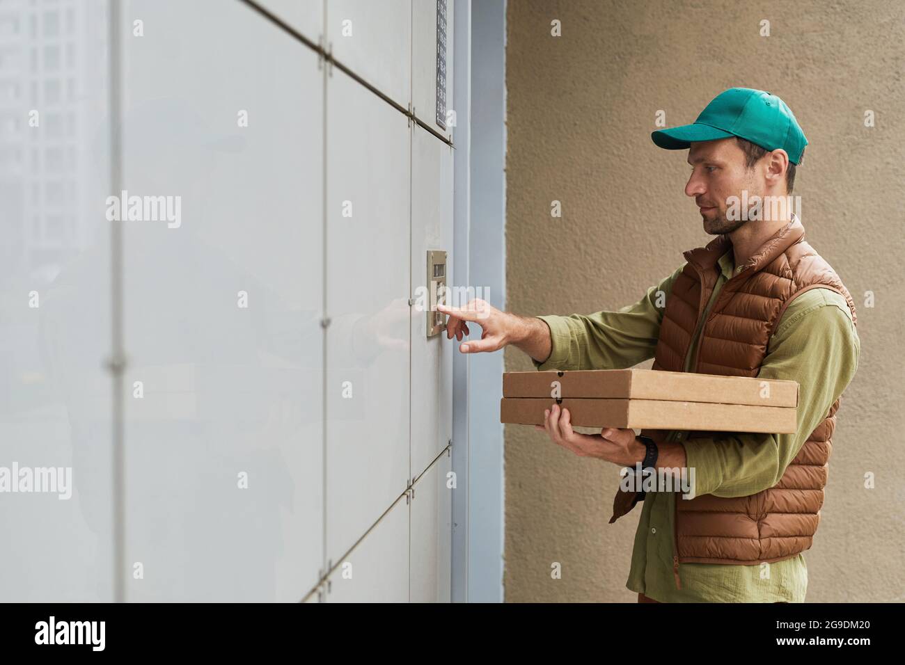Side view portrait of delivery man holding pizza and ringing doorbell, copy space Stock Photo