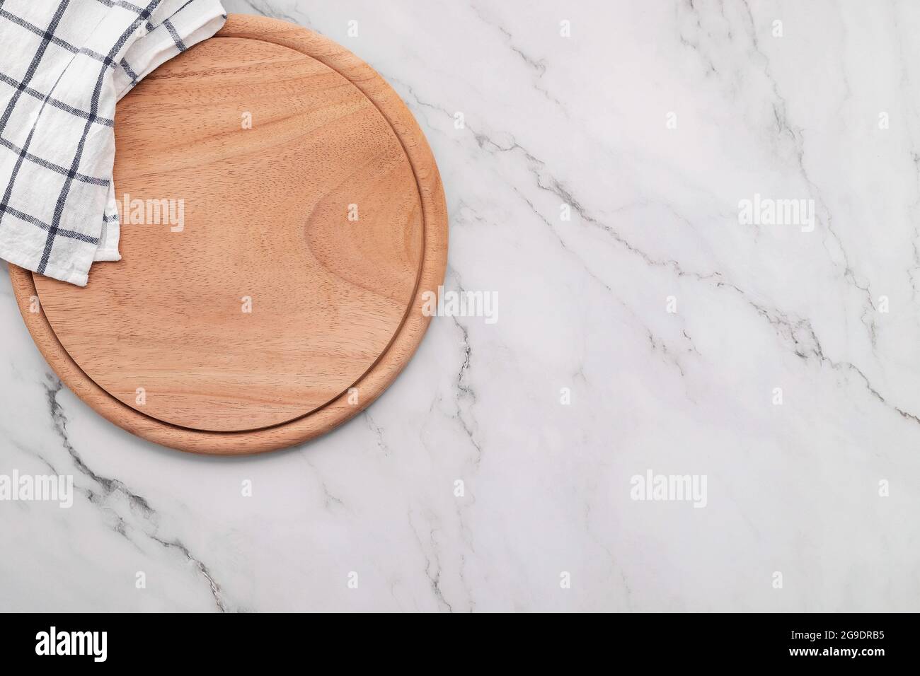 Empty wooden pizza platter with napkin  set up on marble stone kitchen table. Pizza board and tablecloth on white marble background. Stock Photo