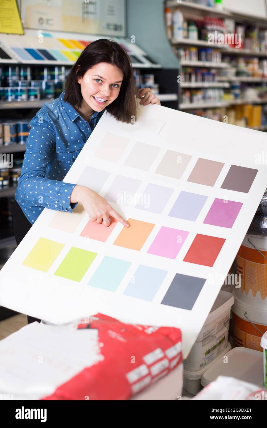 cheerful female customer examining color scheme variants in paint store ...