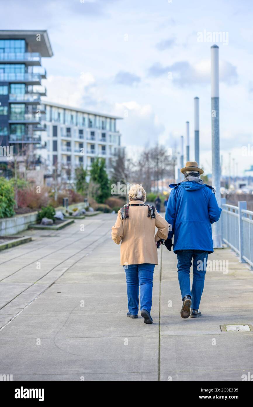 Couple a man and woman are confidently walking along the footpath alley in urban city with multi-storey apartment buildings preferring to move activel Stock Photo