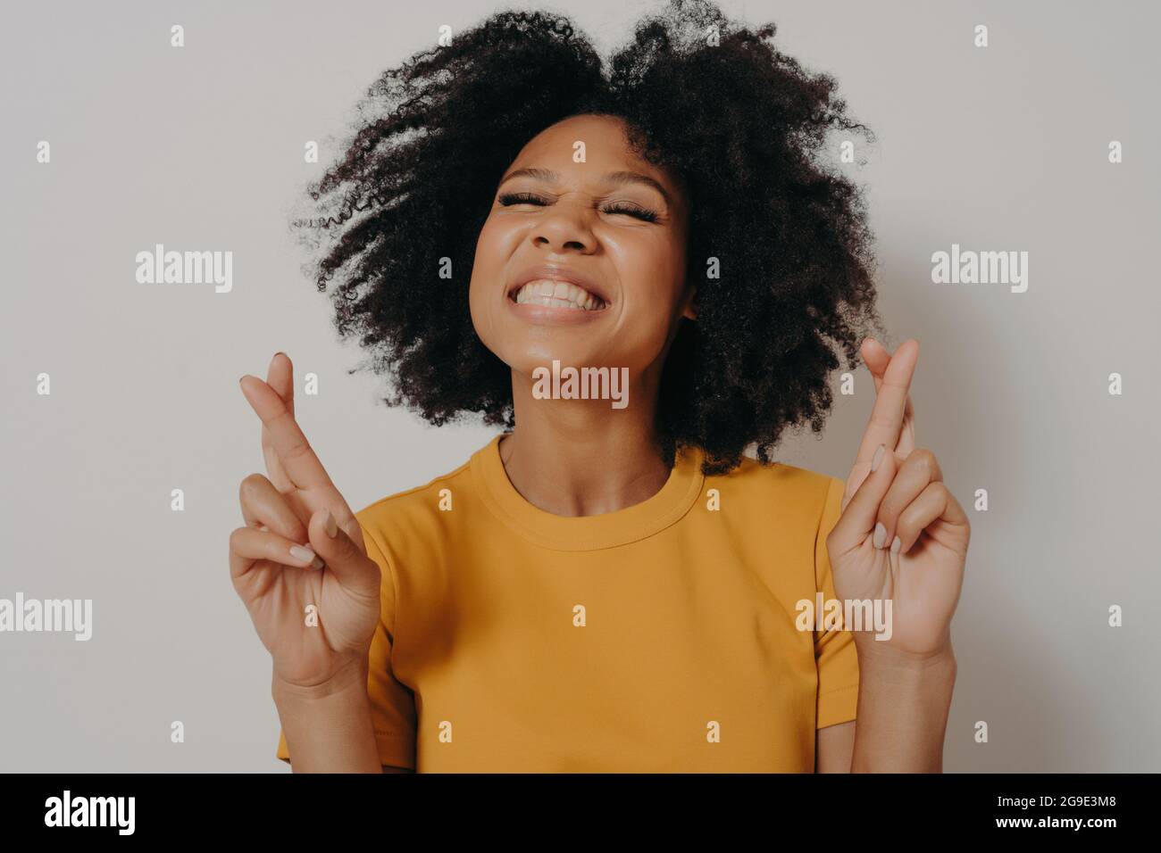 Head shot smiling beautiful African girl with closed eyes crossing fingers wishing good luck Stock Photo