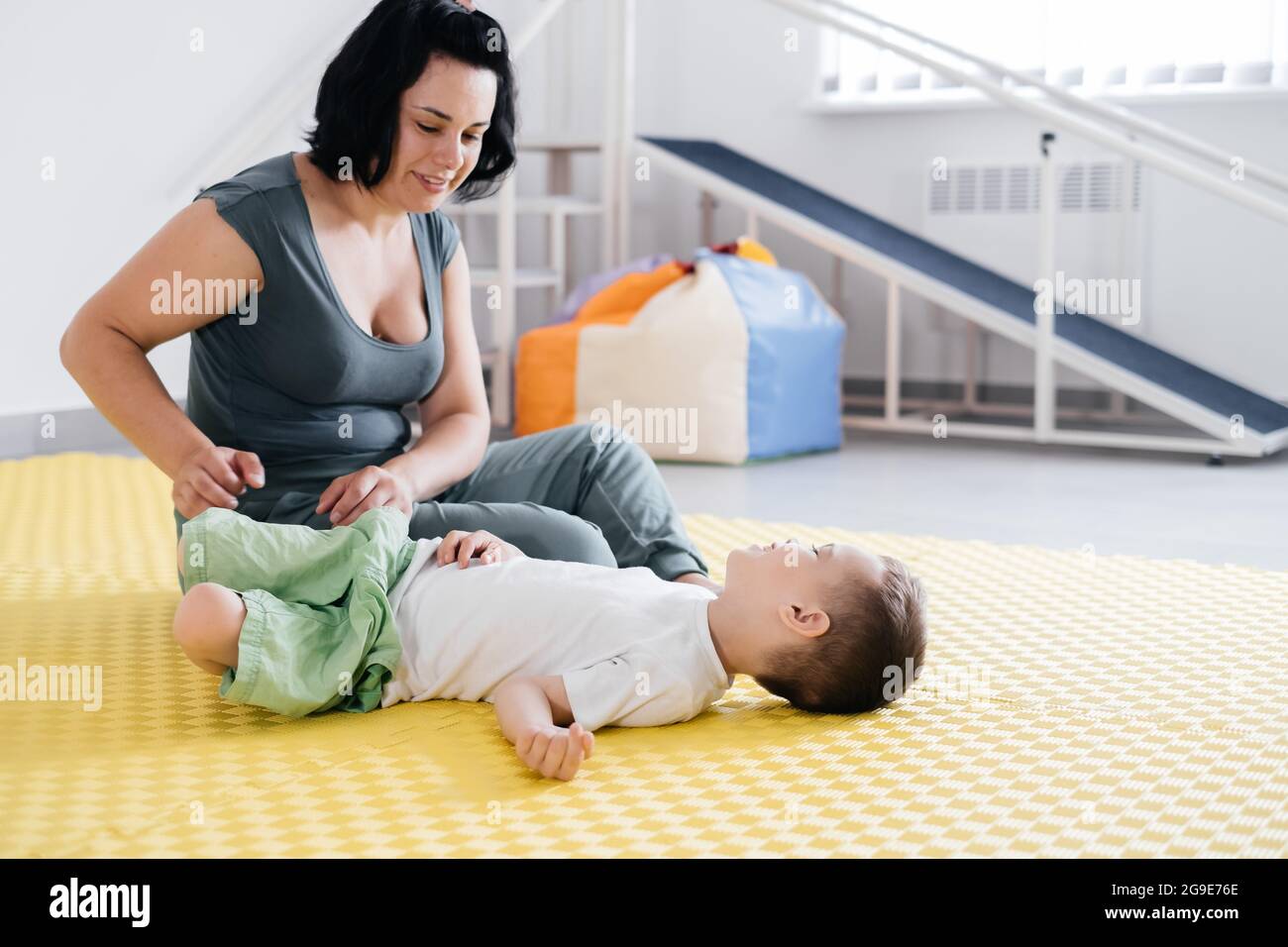 Therapist doing exercises on the mat with disabled child. Boy with