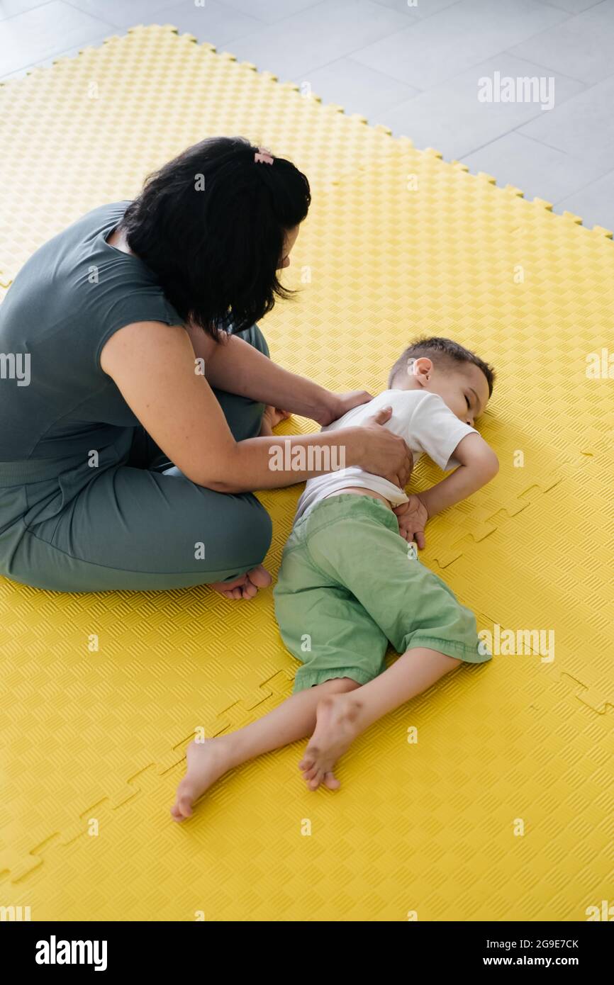 Rehabilitation of children with cerebral palsy. Physical activities for disabled kids in center. Mother, therapist doing exercise with boy on mat Stock Photo