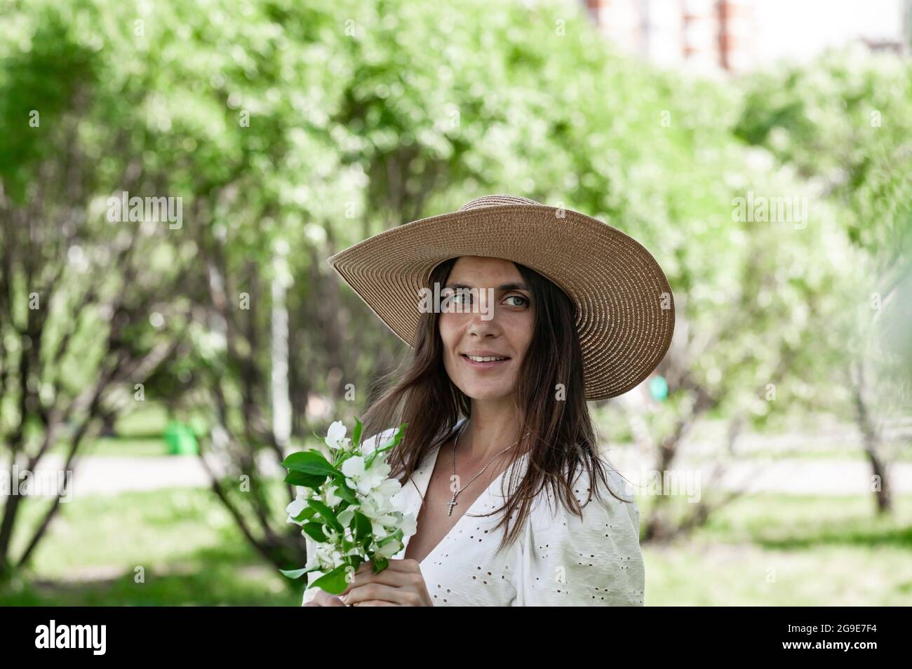 Portrait young smiling woman on the blooming apple trees background. Summer time. Attractive and cute woman is holding apple flower. Pretty and happy Stock Photo