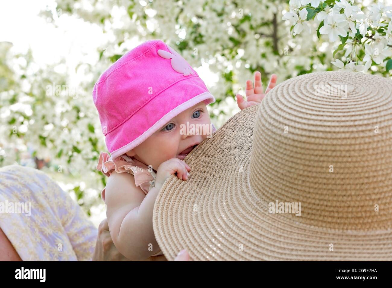 Happy cute and attractive child. Little and pretty girl in hat. Small baby caucasian ethnicity. Woman is holding her daughter in her arms. Stock Photo