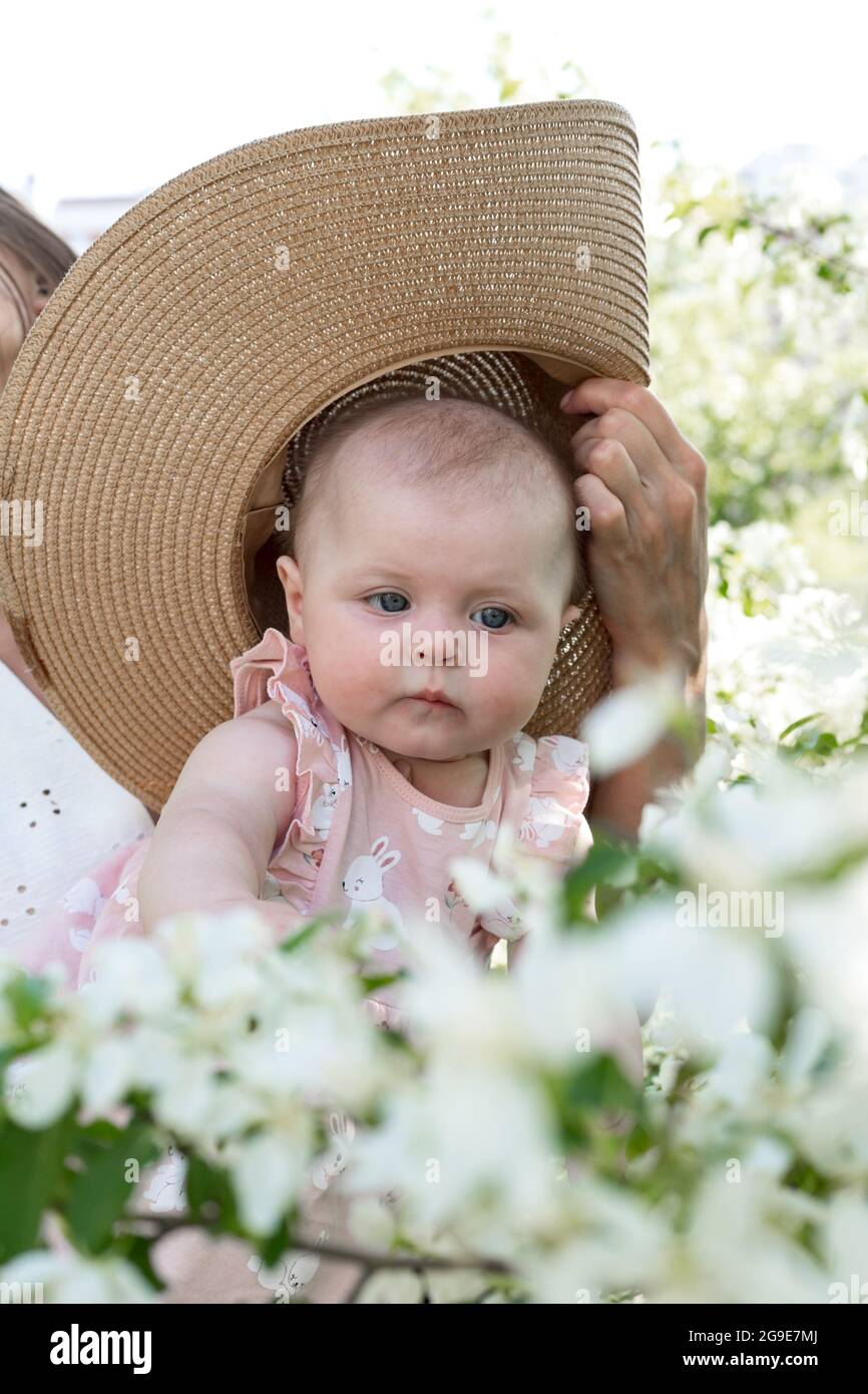 Happy funny and attractive infant girl. Young infant in hat on the tree background. Cute baby caucasian ethnicity with blue eyes. Stock Photo