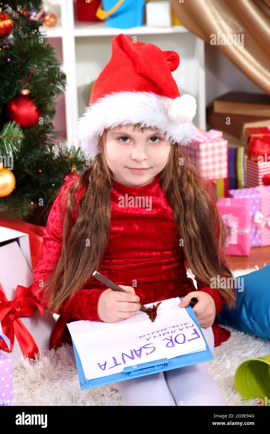 Beautiful little girl in red dress writes letter to Santa Claus in festively decorated room Stock Photo
