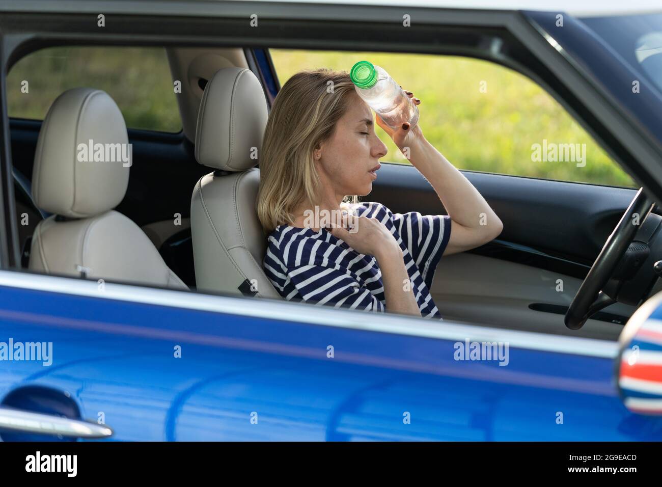 Exhausted girl driver suffering from headache, heat, hot weather applies bottle of water to forehead Stock Photo