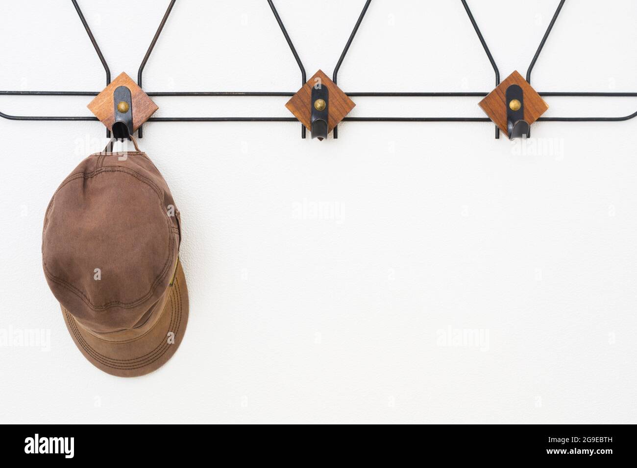 Empty hanger with black metal and wooden elements on white textured wall and cap Stock Photo