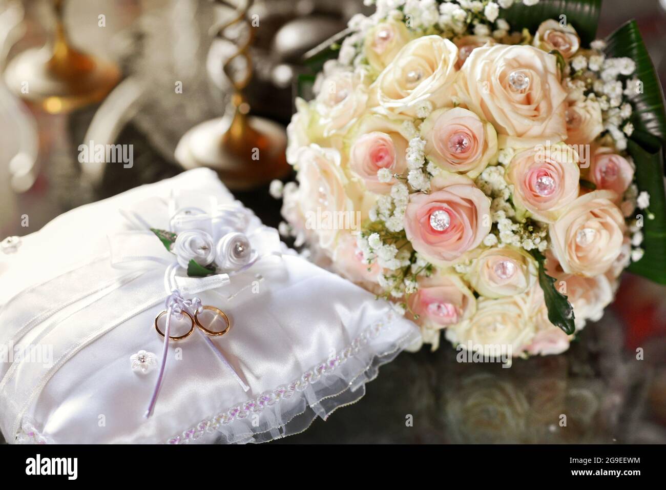 Two gold wedding rings displayed on white cushion with stylish bridal bouquet of pink roses decorated with facetted gems in a love, commitment and rom Stock Photo