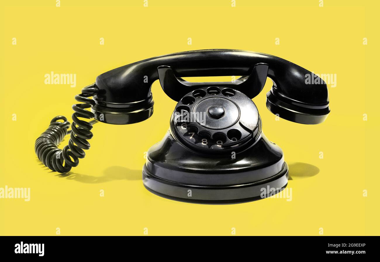 Retro black rotary dial-up telephone instrument with a handset on a cradle in a telecommunications concept on a yellow background Stock Photo