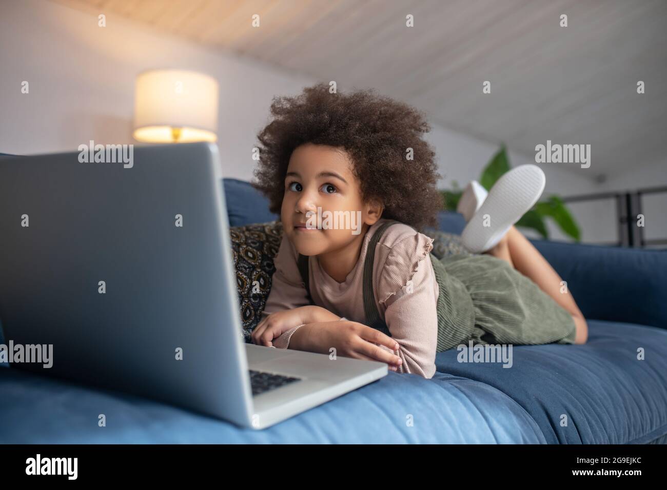 Little girl lying on couch near laptop Stock Photo - Alamy