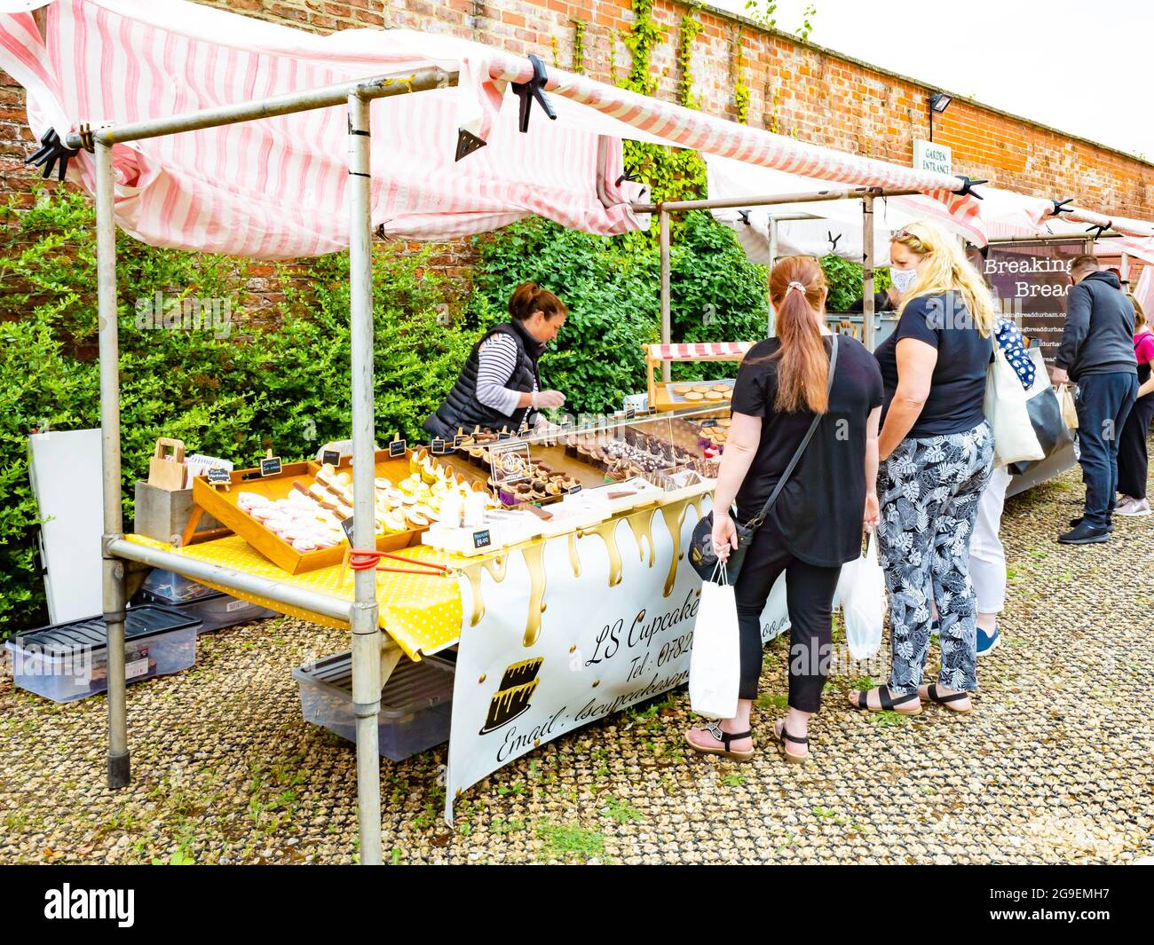 A woman stall holder at a farmer's market at the Walled Rose Garden Wynyard Hall serving cupcakes and other confectionery Stock Photo