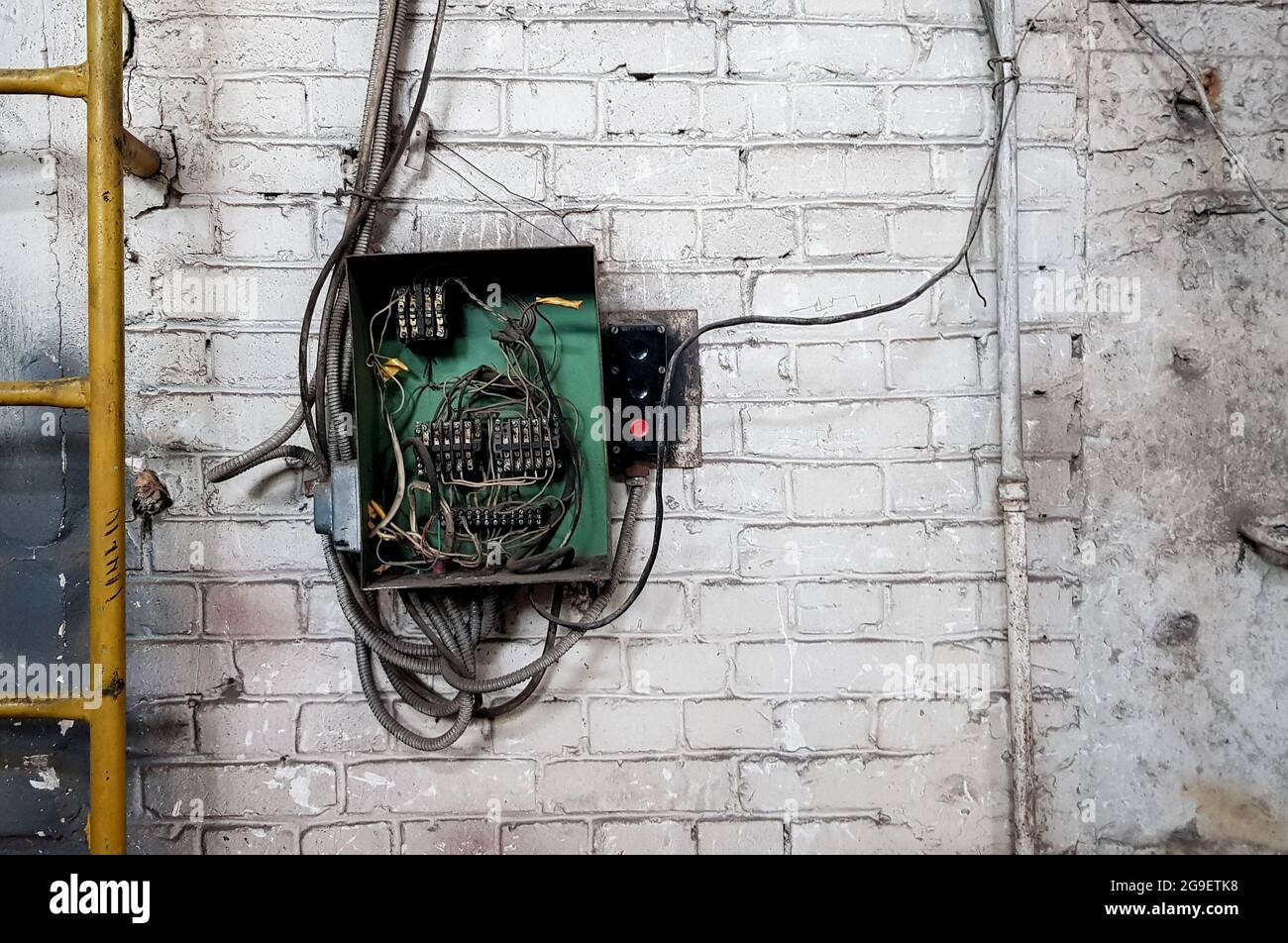 Old electrical panel on the wall of the house. Electric cables stick out from the electric panel on the white brick wall of the old house Stock Photo