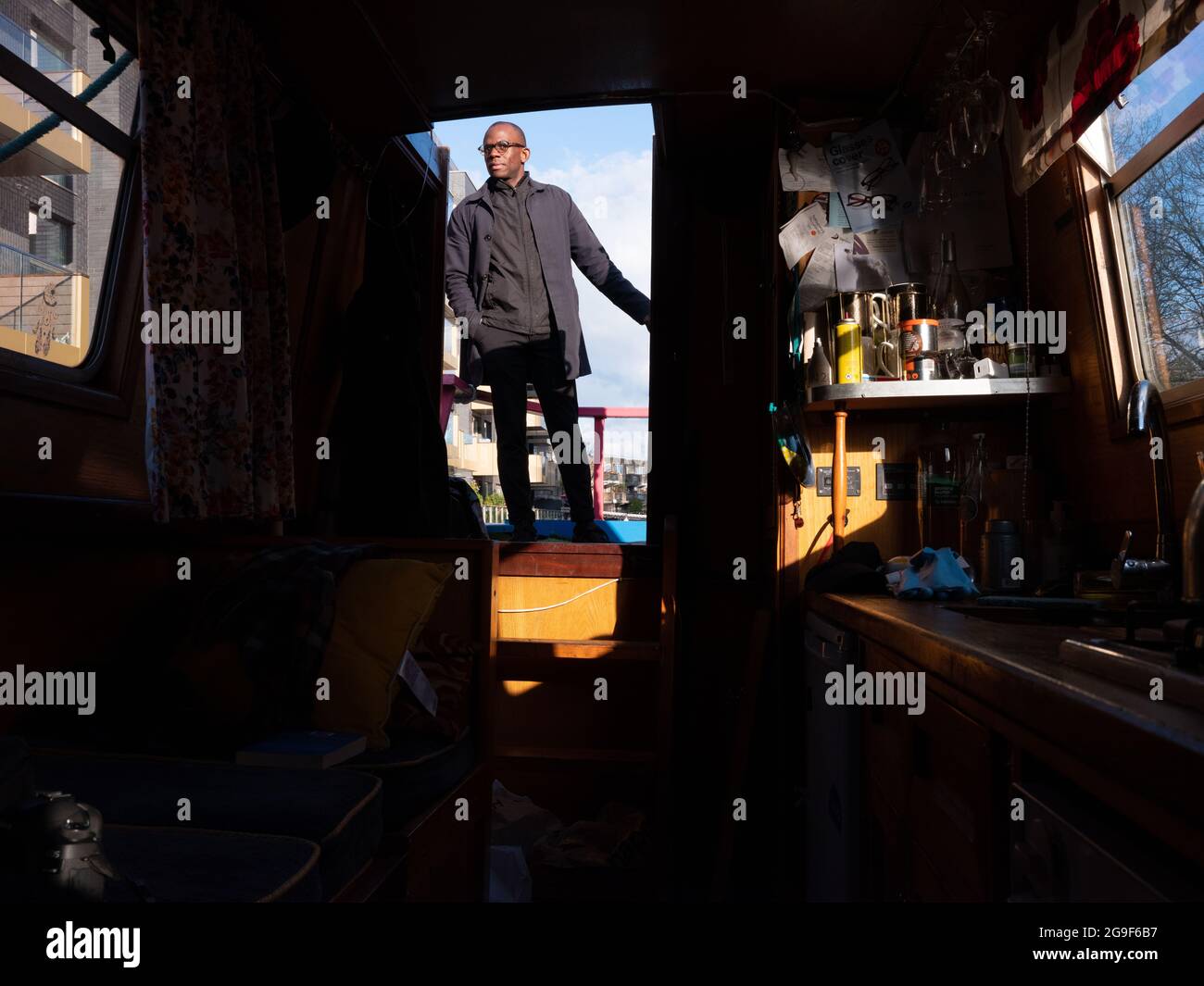 A black man steering a narrow boat with a tiller along the Regent’s Canal in Little Venice, London. Stock Photo