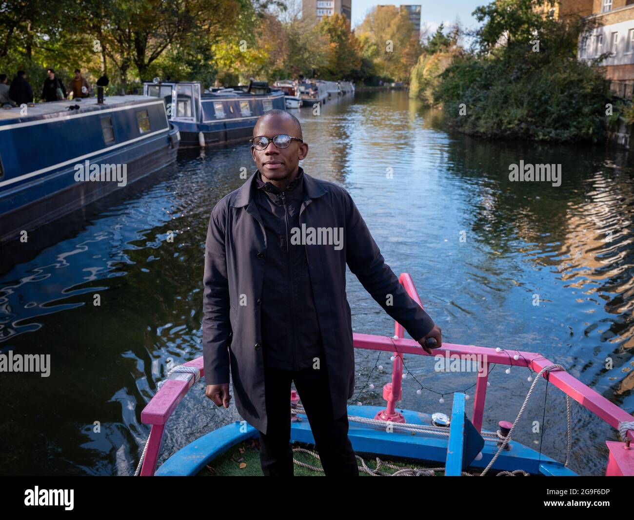 A black man steering a narrow boat with a tiller along the Regent’s Canal in Little Venice, London. Stock Photo
