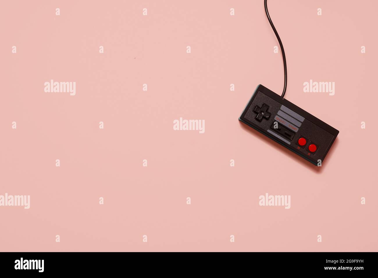 Retro vintage black game console controller on a pastel pink background with copy space and room for text. Stock Photo