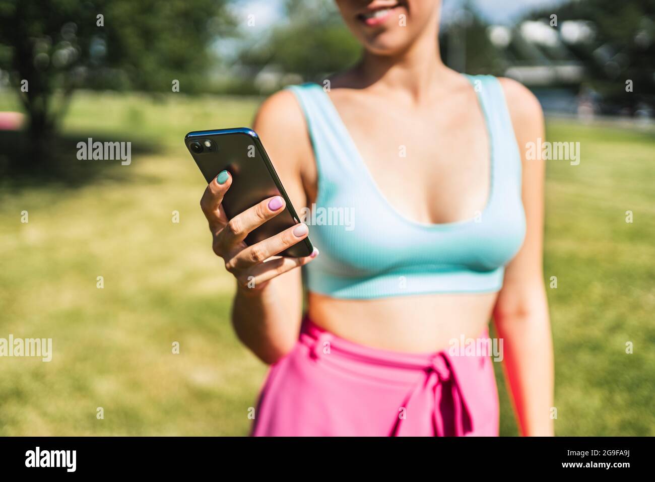 Girl using phone and texting in summer in outdoor park. Woman looking sms message with smartphone. Fit person with cellphone outside in garden. Stock Photo