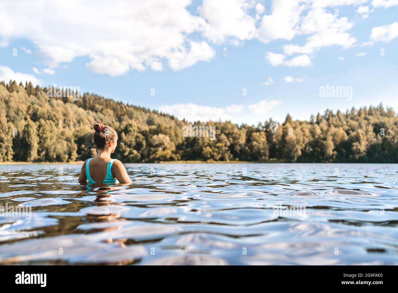 Lake in Finland. Woman swimming. Finnish nature, water and serene sky in summer. Outdoor bathing in Scandinavia after sauna. Green forest and beach. Stock Photo