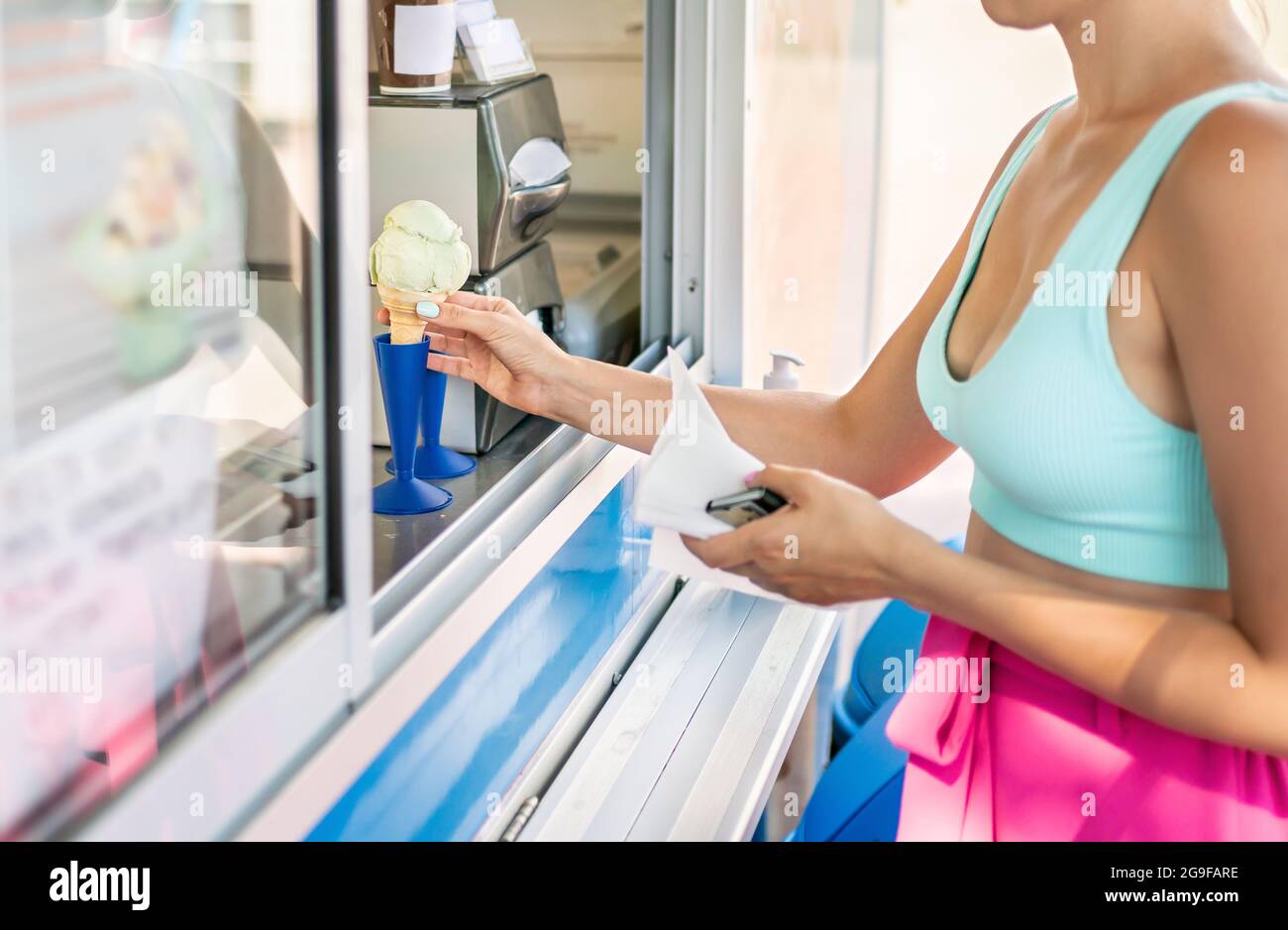 Buying ice cream cone from parlor or kiosk. Customer holding icecream in hand. Gelato truck, van or dessert shop. Gelateria in city street. Stock Photo