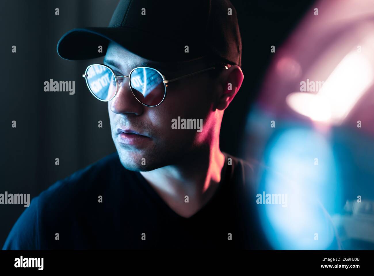 Neon light in glasses of a man. Futuristic cyber studio portrait. Techno glow and vibrant cyberpunk color. Male model with sunglasses. Stock Photo