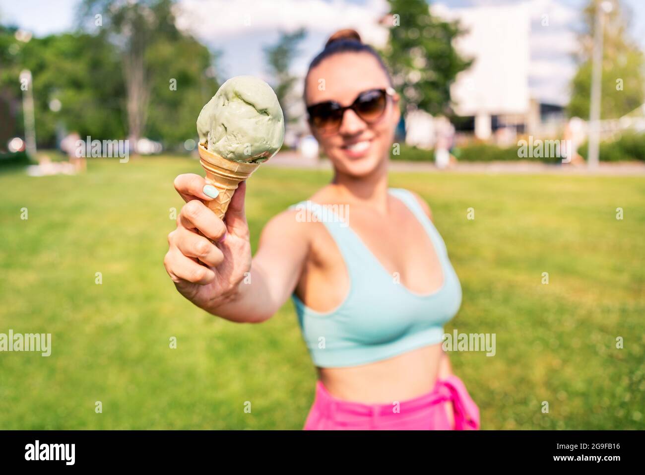 Fit slim woman showing ice cream cone in city park in summer. Happy smiling portrait of young laughing model and melting icecream. Stock Photo