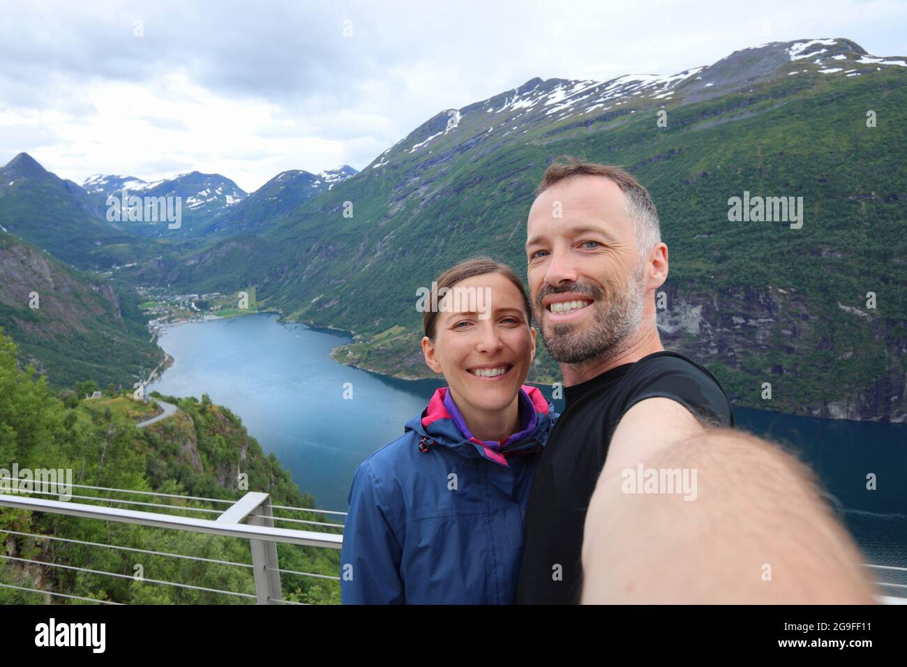 Couple traveler selfie in Norway hiking area - mountain view above Geiranger fjord. Outdoor recreation activity. Stock Photo
