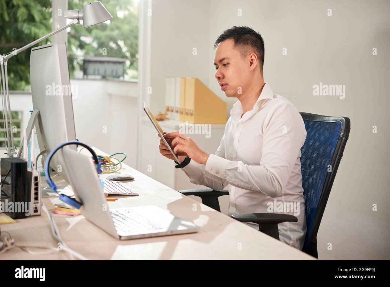 Young software engineer sitting at office desk and testing new application he was working on on tablet computer Stock Photo