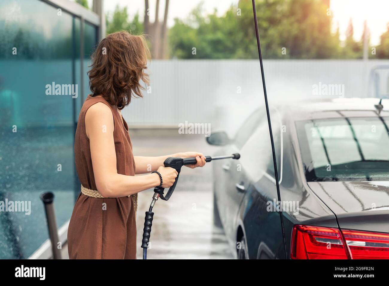 Side view young adult woman washing car with high pressure water
