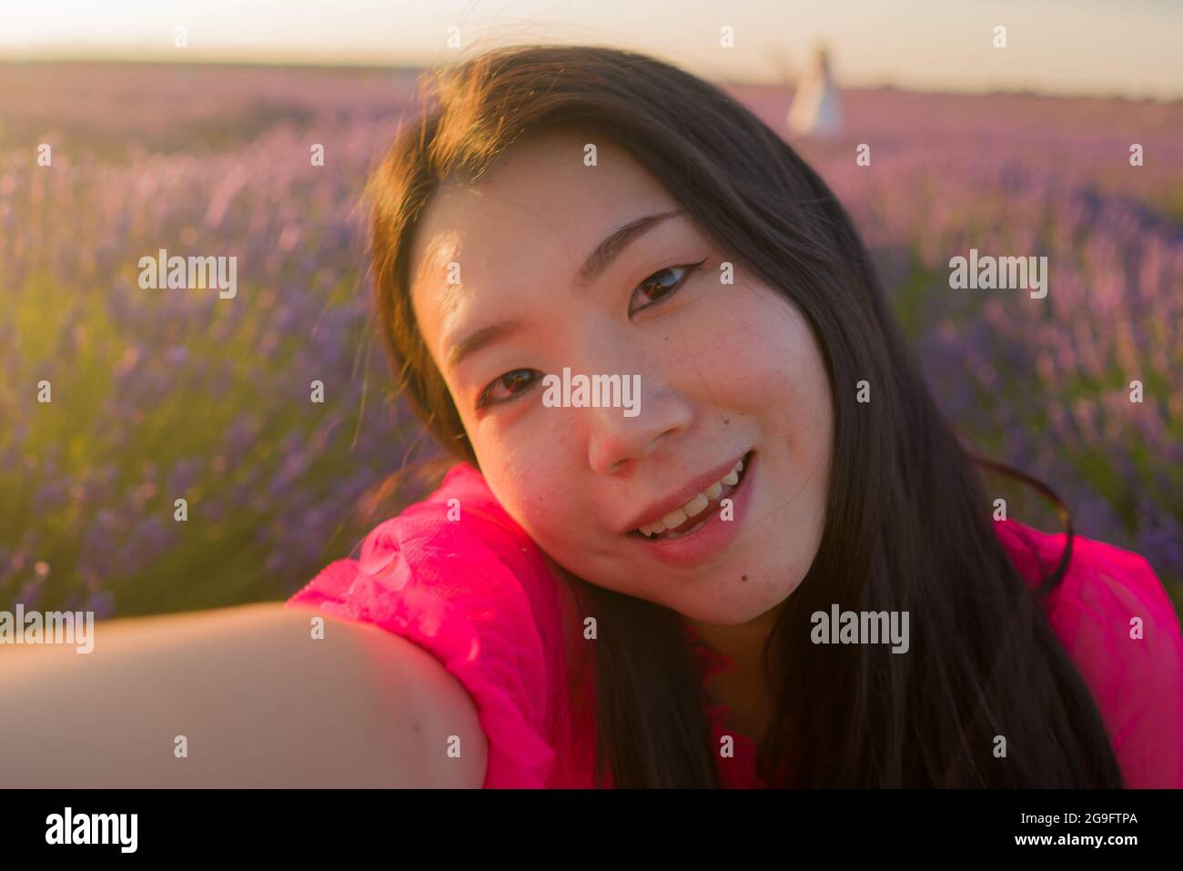young happy and beautiful Asian Chinese woman in Summer dress taking sunset selfie with mobile phone at purple lavender flowers field in nature and ro Stock Photo