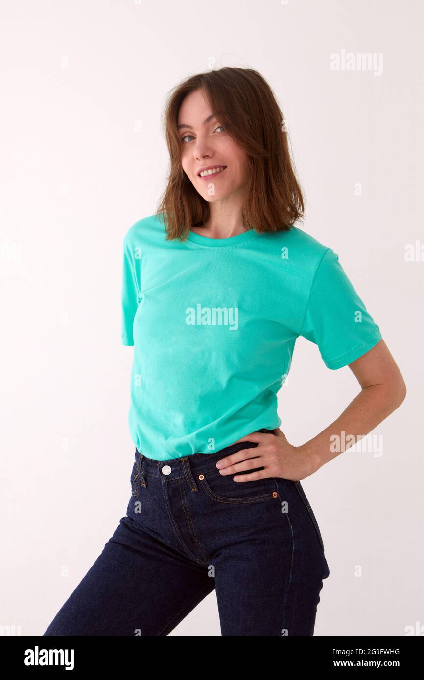 Positive female model wearing t shirt and jeans standing with hands on waist against white background and looking at camera Stock Photo