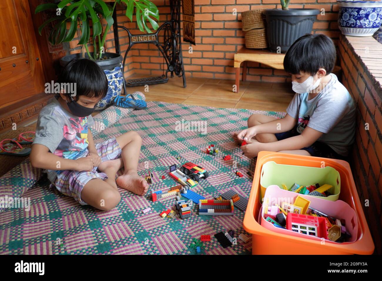 Two boys with facemask play lego toys together in their house. Stock Photo