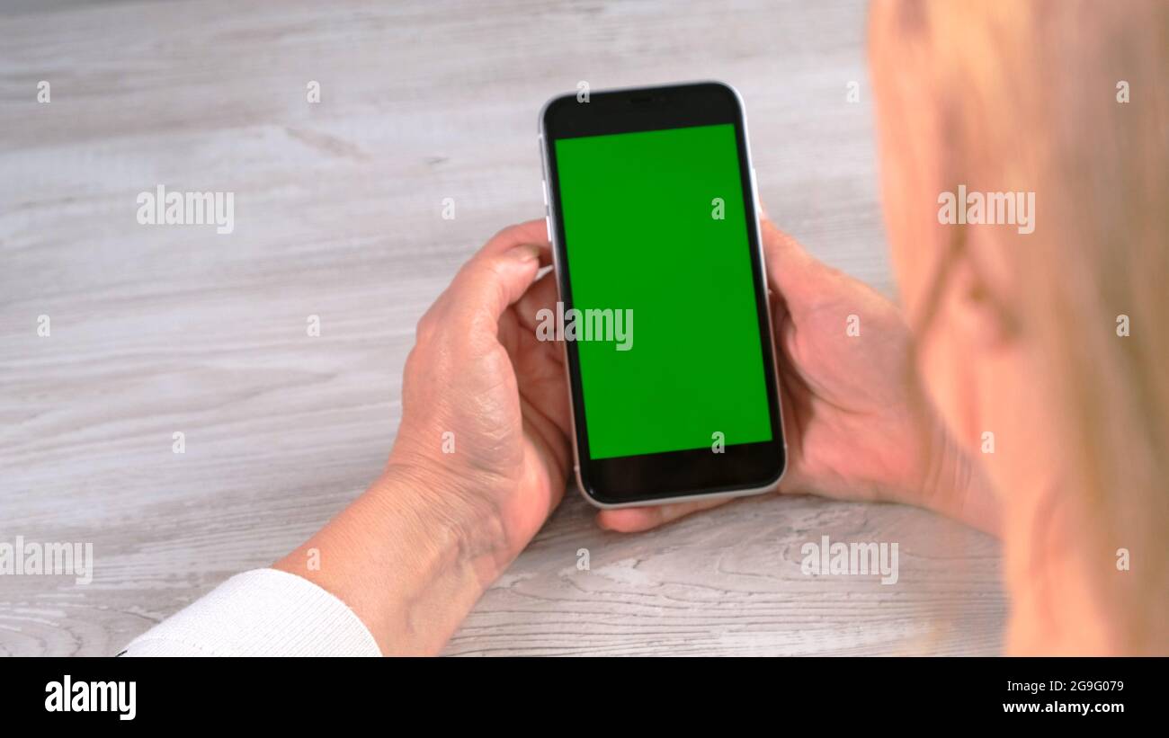 Middle-aged female senora uses an iPhone smartphone with a chroma key screen, copy space. Online shopping concept, use of mobile applications: Moscow Stock Photo