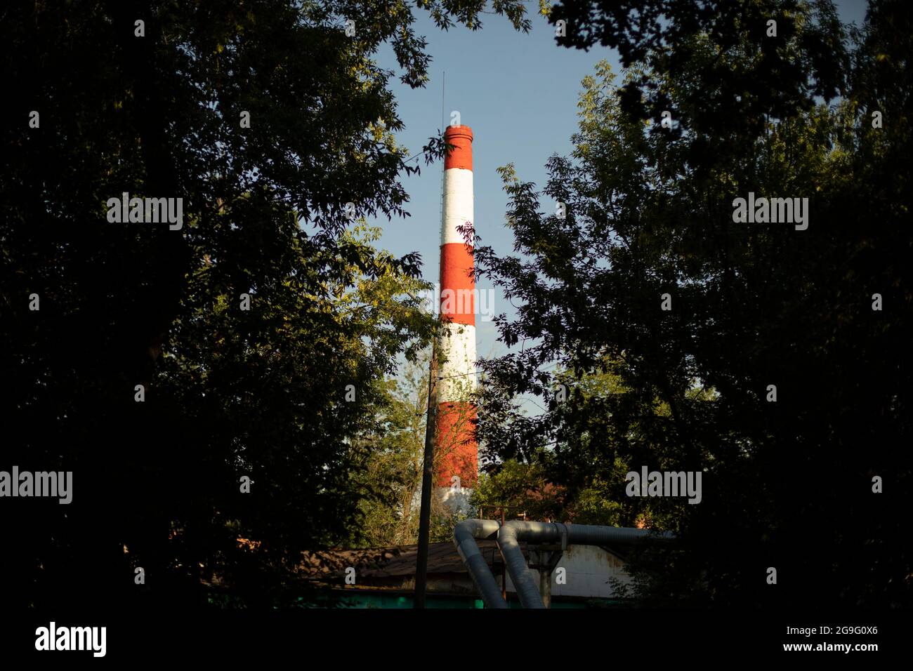 Industrial pipe of the boiler station. Red and white chimney in the city. Brick pipe for steam removal. Stock Photo