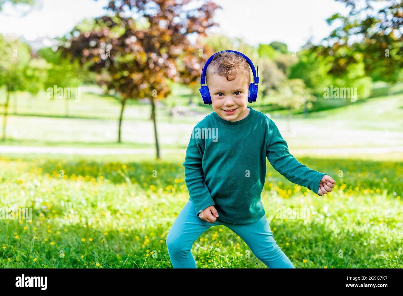 happy young kid listening to music outdoor in a park. smiling little child dancing outside in a garden wearing headphones and making fake guitar play Stock Photo