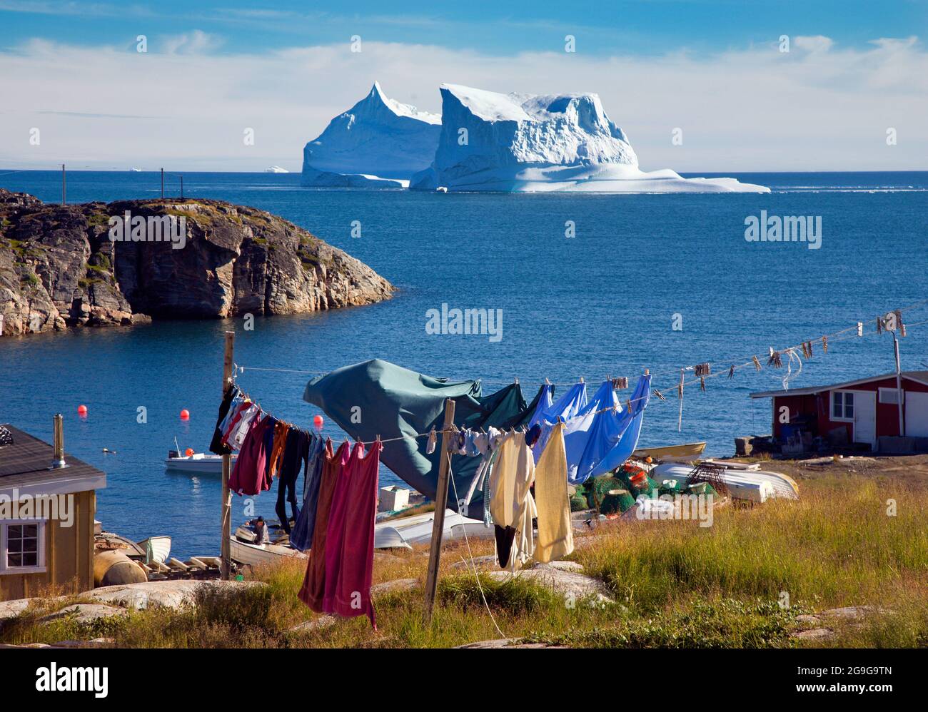 A large iceberg grounded in a bay just off the west coast town of Qeqertarsuaq, Greenland, with a washing line in the foreground and clothes drying Stock Photo