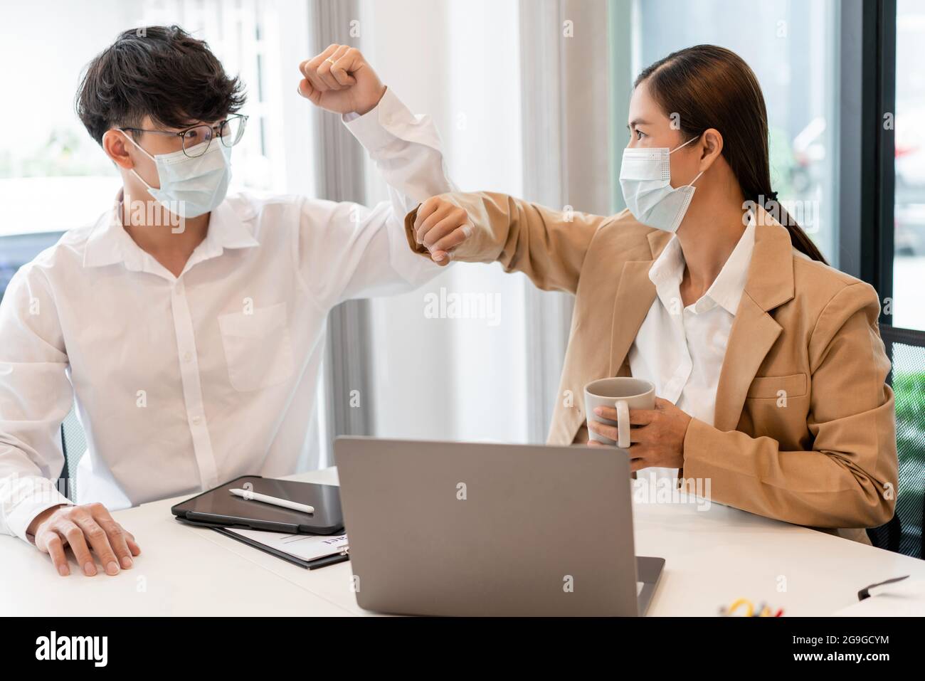 two business partners wearing protective mask touching elbows together