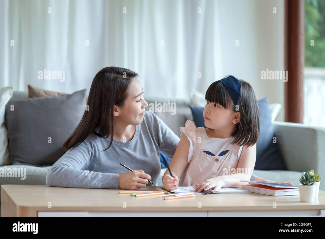 Asian mother teaching her cute kid daughter to studying in living room at home Stock Photo