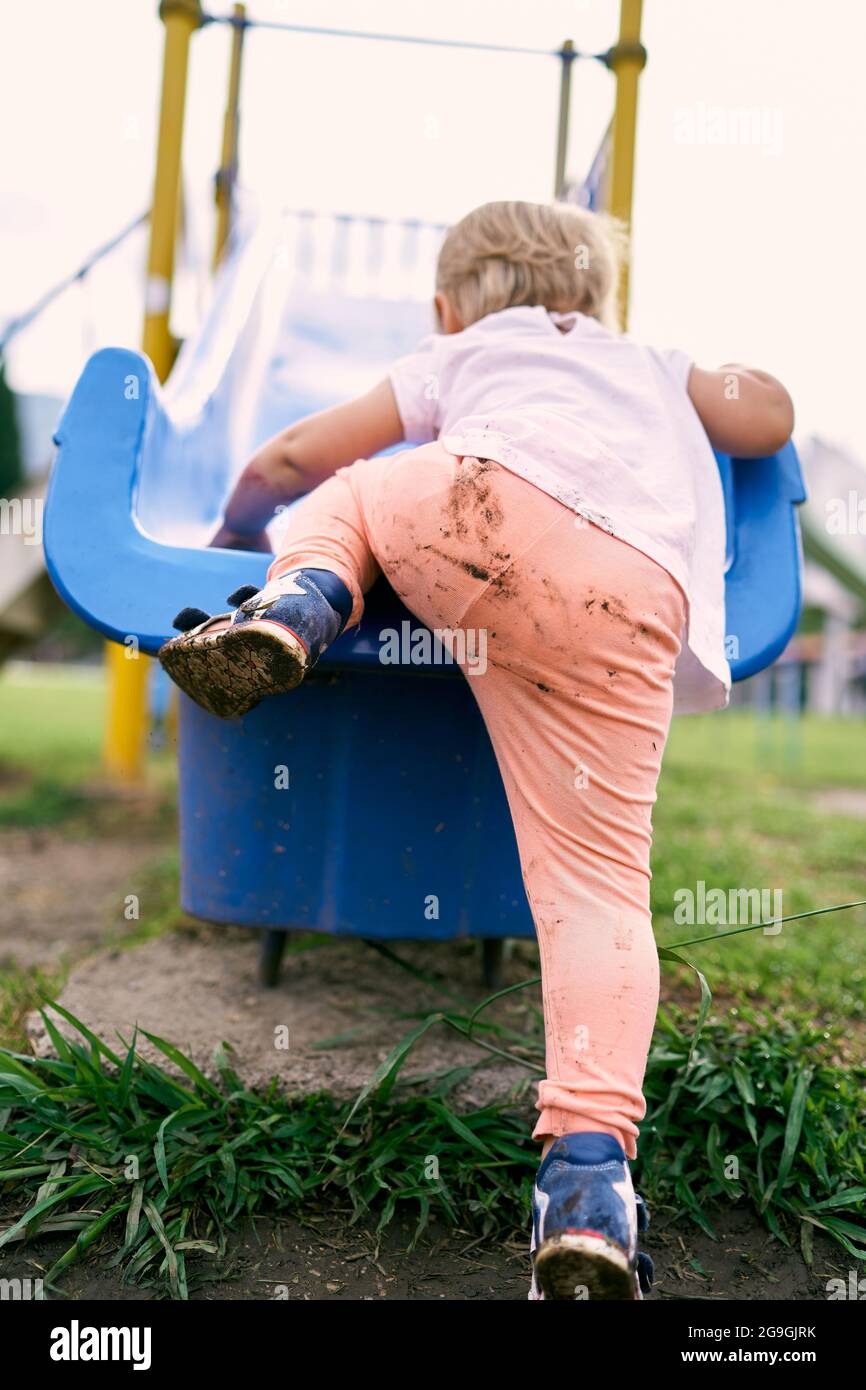Small child in mud-stained pants climbs a slide. Close-up Stock Photo