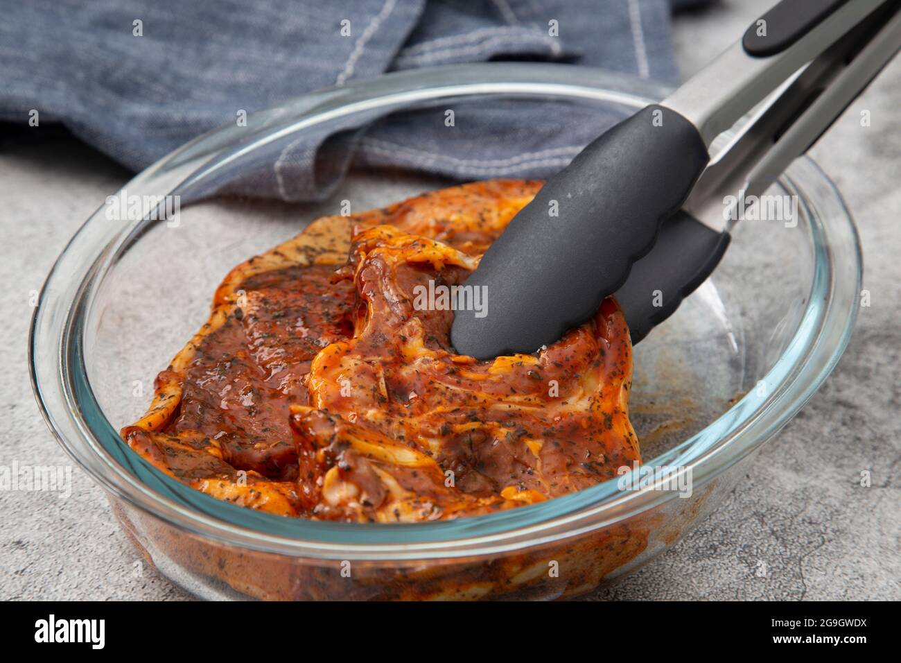 Lamb chops with a mint sauce marinade in a glass dish with kitchen tongs and tea towel. On a