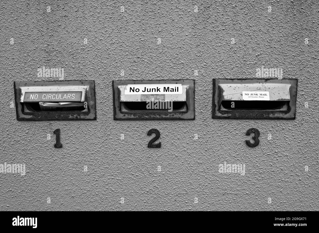 No Circulars, No Junk Mail signs, 3 mail box slots, rough cement wall, text, words, black and white, Auckland, New Zealand Stock Photo