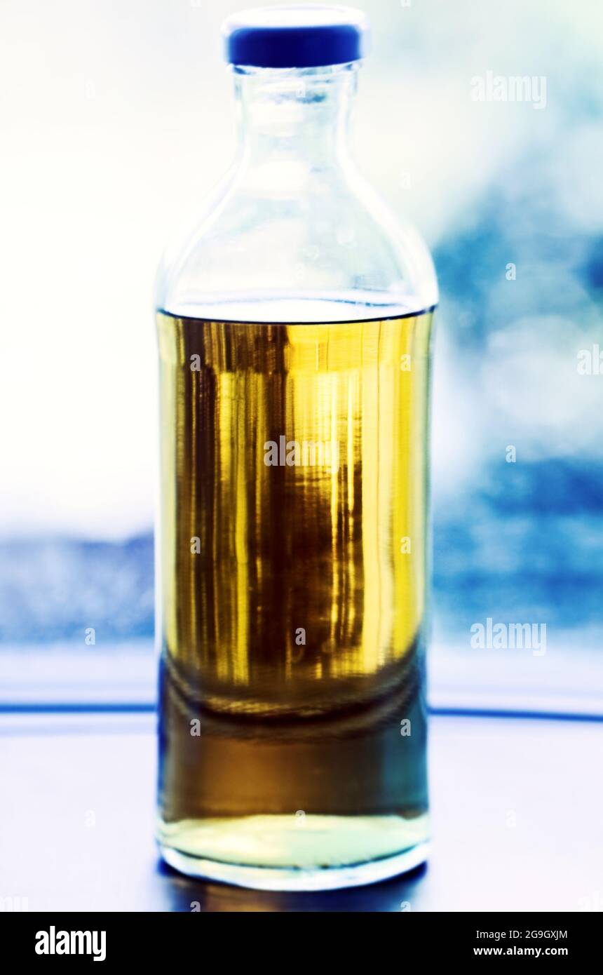 Real clear glass bottle with yellow liquid at light blue background Stock Photo