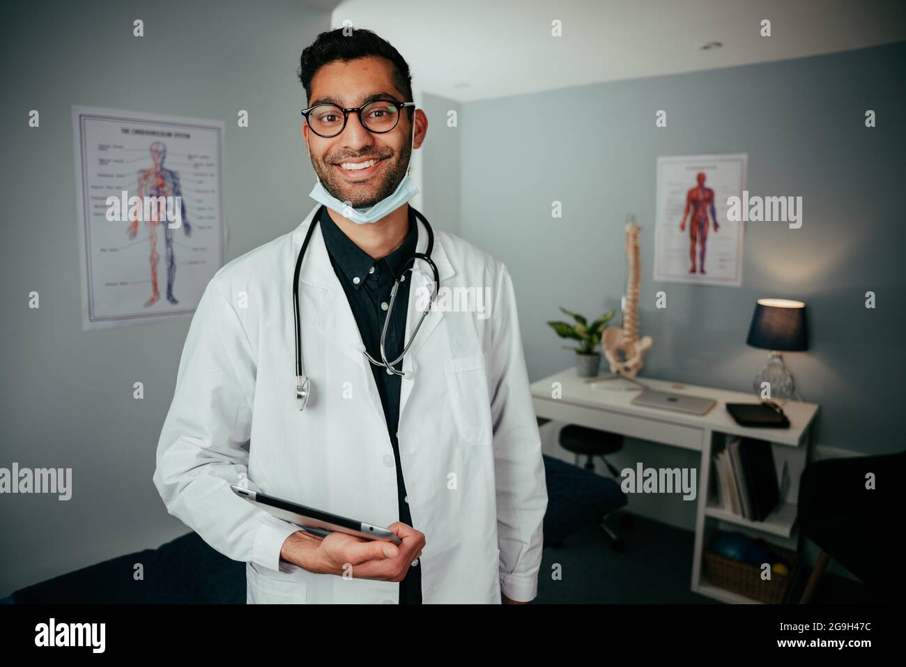 Mixed race male doctor working in office smiling while holding digital tablet Stock Photo