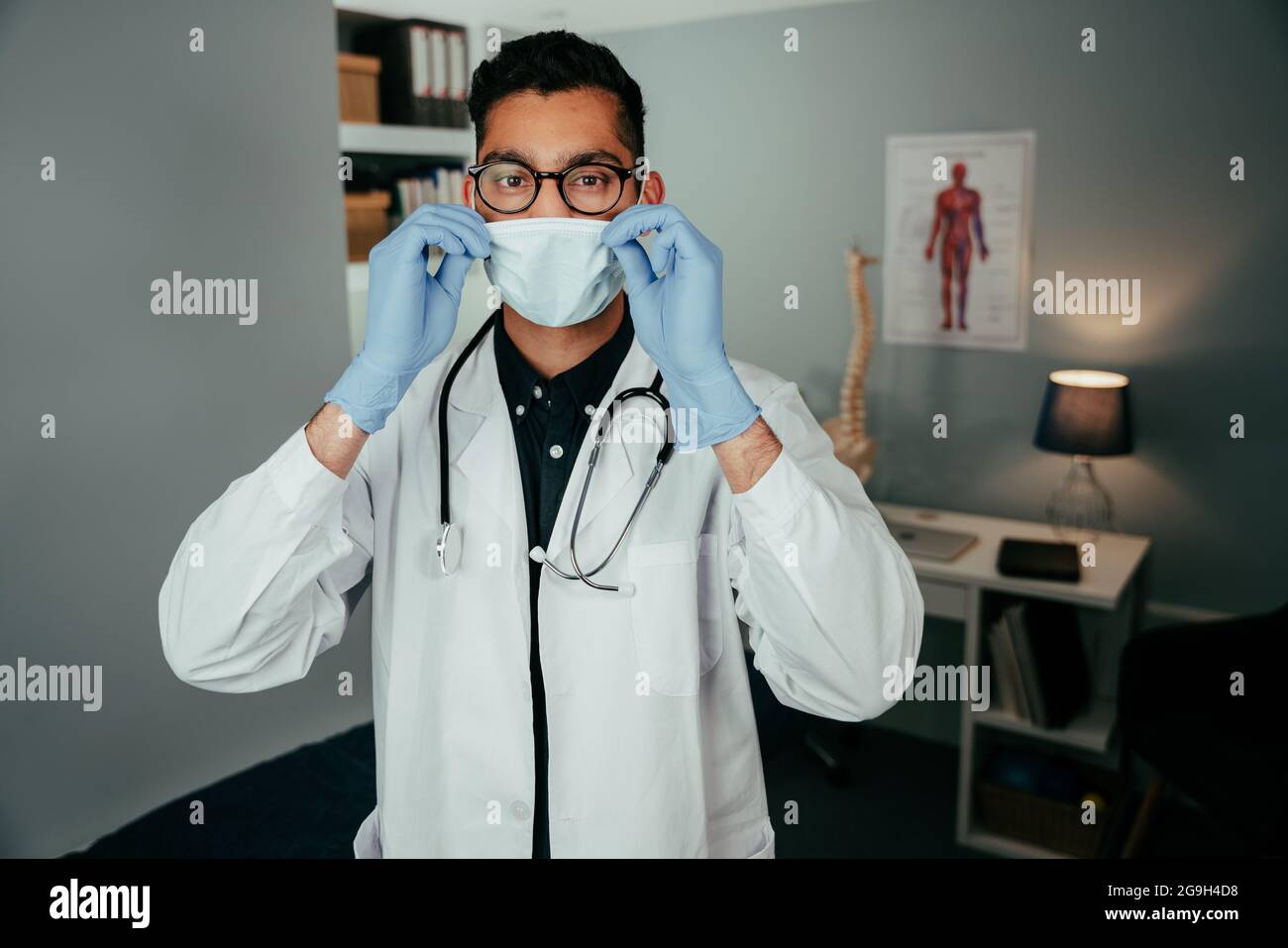 Mixed race male doctor working in office wearing surgical mask Stock Photo